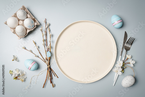Happy Easter composition for easter design. Elegant Easter eggs, plate and flowers on pastel blue background. Flat lay, top view, copy space.