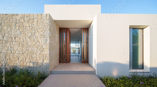 Contemporary house entryway featuring natural stone wall, wooden door, and clear sky in the morning light photo