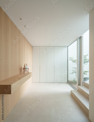 A minimalist interior with light wooden panels, white walls, and a large window providing ample natural light. A small wooden bench with a backrest is placed against the wall photo