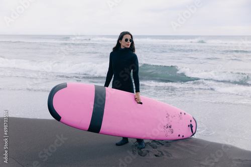 Extreme surfer woman in wetsuit with surfboard go to winter surfing in Atlantic ocean Kamchatka Russia. Adventure travel sport concept