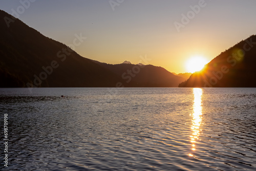 Breathtaking allure of sunset at alpine lake Weissensee in remote Austrian Alps in Carinthia. Embrace serene ambiance as tranquil surface of water amplifies sun gentle rays. Sun gracefully descends