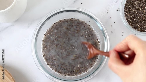 Hand mixing chia seeds and plant-based milk in a bowl to prepare vegan pudding. Top table view. Healthy breakfast food preparation concept. photo