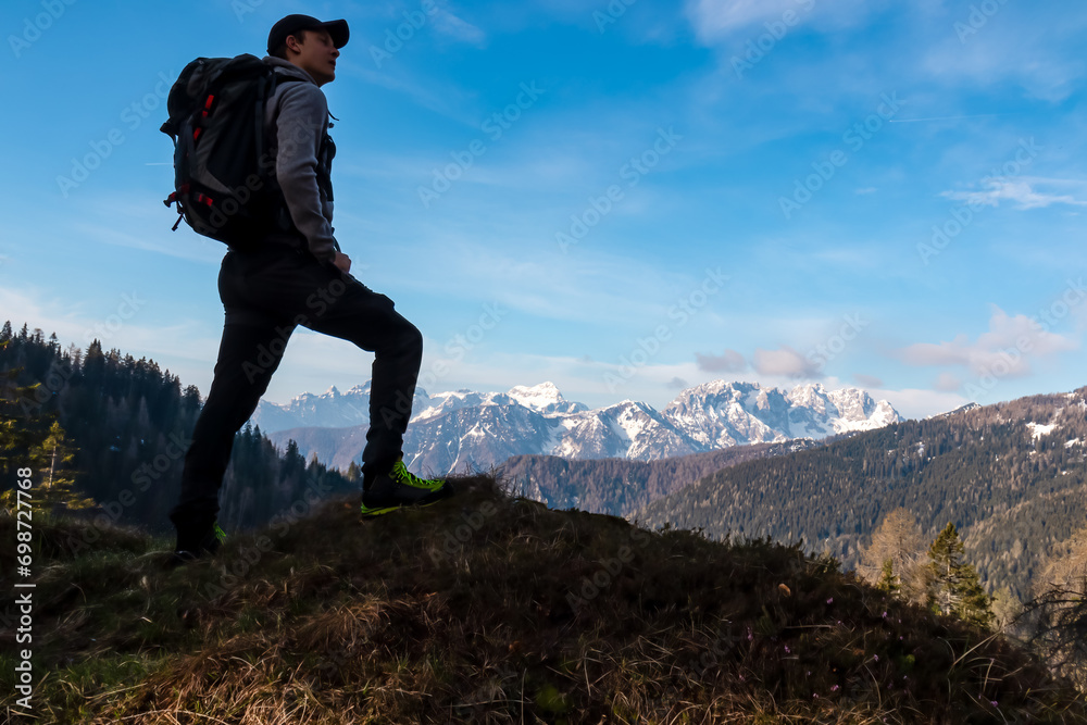 Hiker man with scenic view of snow covered mountain range Julian Alps seen from Karawanks in Carinthia, Austria. Looking at mountain peak Triglav. Tranquility in Slovenian Austrian Alps. Wanderlust Hiker man with scenic view of snow covered mountain range Julian Alps seen from Karawanks in Carinthia, Austria. Looking at mountain peak Triglav. Tranquility in Slovenian Austrian Alps. Wanderlust