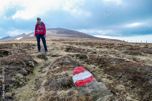 Hiker woman next to path mark with panoramic view of mountain peak of Amerinkogel on Packalpe, Lavanttal Alps in Styria, Austria. Remote alpine hill landscape in Austrian Alps. Tranquil scene photo