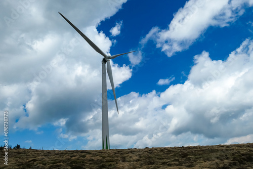 Wind turbine with its blades spinning in the wind. The turbine is mounted on a tall tower and is surrounded by clouds in the sky. Renewable energy on Packalpe in Styria, Austria, Austrian Alps. photo