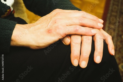 Übereinanderliegende schlanke Männerhände stützen sich ab auf Knie von sitzendem Mann mit schwarzer Jeanshose in Raum  photo