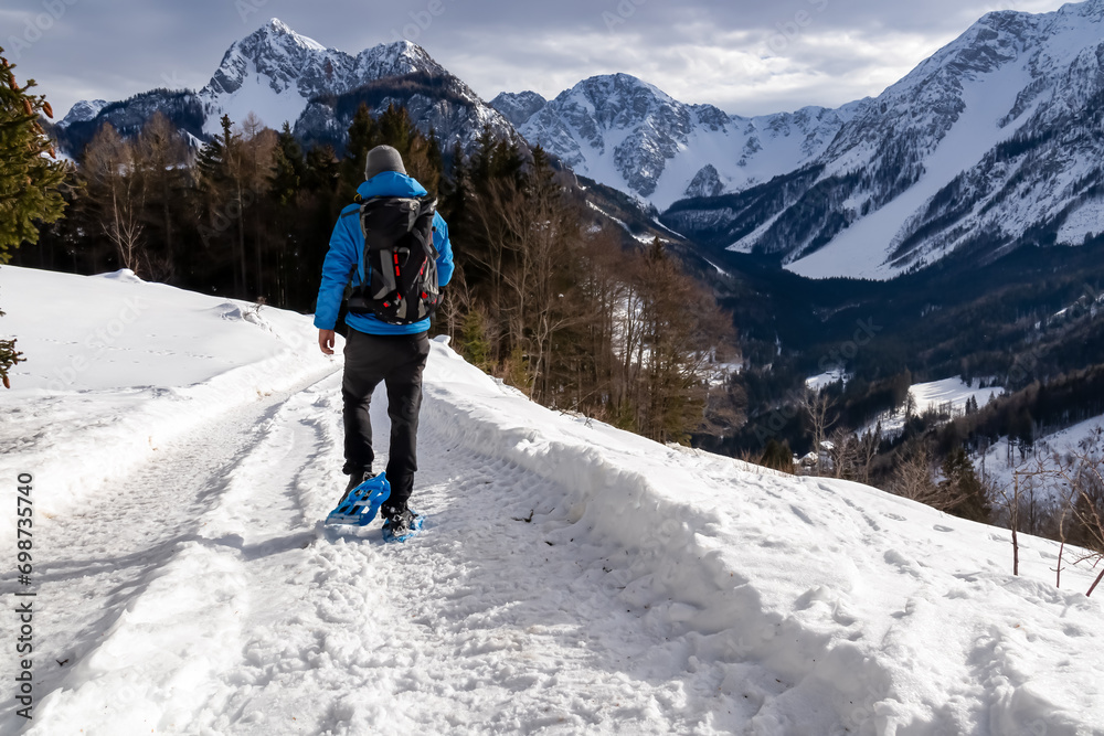 Man in snow shoes on hiking trail with panoramic view on snow capped mountain peaks of Karawanks, Carinthia, Austria. Looking at summits Kosiak and Hochstuhl, Austrian Alps. Alpine landscape in winter Man in snow shoes on hiking trail with panoramic view on snow capped mountain peaks of Karawanks, Carinthia, Austria. Looking at summits Kosiak and Hochstuhl, Austrian Alps. Alpine landscape in winter