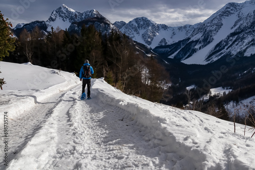 Man in snow shoes on hiking trail with panoramic view on snow capped mountain peaks of Karawanks, Carinthia, Austria. Looking at summits Kosiak and Hochstuhl, Austrian Alps. Alpine landscape in winter