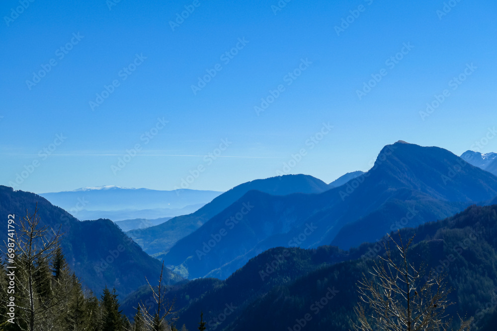 Panoramic view of misty Karawanks mountain range on sunny day in Carinthia, Austria. Remote high alpine landscape in Bodental, Austrian Alps. Outdoor pursuit. Dreamy tranquil hiking trail in forest