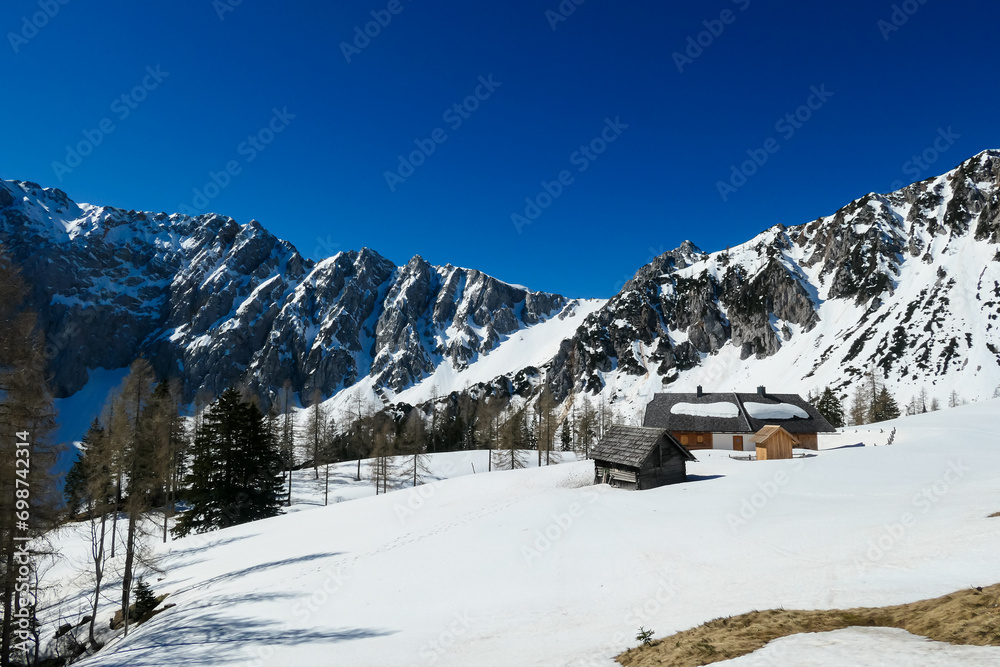 Snow covered Ogrisalm with a panoramic view on mountain peaks in early spring in Karawanks, Carinthia, Austria. Remote alpine cottage. Looking on mount Vertatscha and Hochstuhl