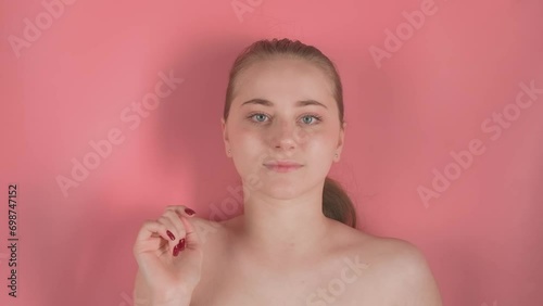 On a pink background is a pretty girl without makeup. She lies supposedly underwater, looks into the camera. Then she touches the water with her hand. that starts to move at the touch photo