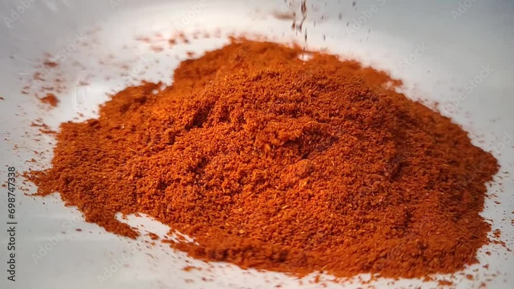 Organic spicy red hot chilli pepper powder or dust falling on a pile of cayenne pepper powder isolated and scattered on a white background surface. Closeup macro slow motion view. Organic spicy red hot chilli pepper powder or dust falling on a pile of cayenne pepper powder isolated and scattered on a white background surface. Closeup macro slow motion view.