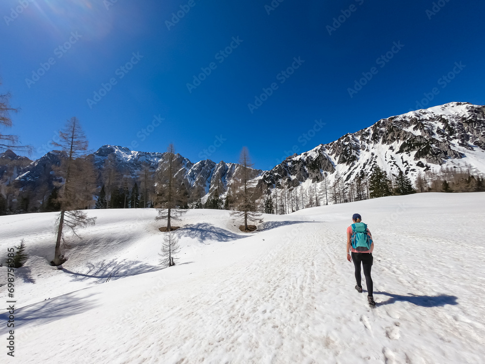 Woman on snow covered hiking trails with scenic view of Karawanks mountains in Carinthia, Austria. Looking at snow capped summit of Vertatscha and Hochstuhl. Remote alpine landscape in Bodental