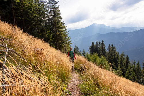 Woman with backpack on hiking trail along golden colored blades of grass in mountain ranges of Karawanks in Carinthia, Austria. Remote alpine landscape in Bodental, Austrian Alps. Wanderlust in autumn photo