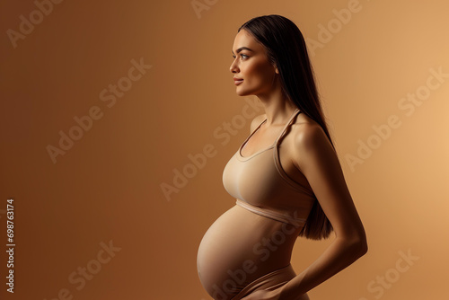 pregnant woman in beige sports bra on a pastel brown background, studio portrait