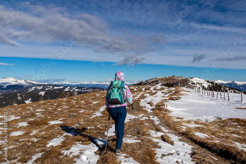 Woman with hiking backpack walking on snow covered alpine meadow on trail from Ladinger Spitz to Geierkogel, Saualpe, Lavanttal Alps, Carinthia, Austria. Snow capped mountain ranges of Austrian Alps