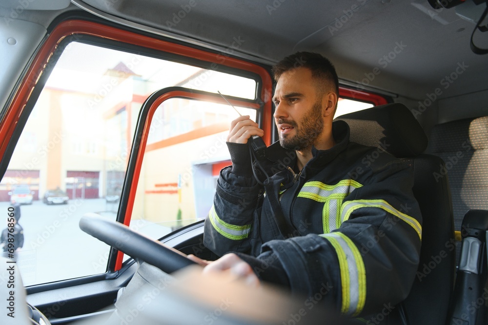 Firefighter using radio set while driving fire truck - obrazy, fototapety, plakaty 