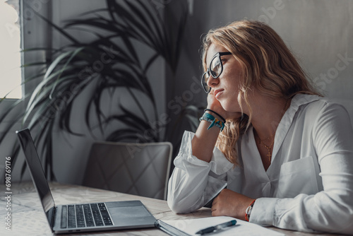 Obraz na plátne Discontented thoughtful woman with hand under chin bored at work, looking away sitting near laptop, demotivated office worker feels lack of inspiration, no motivation, boring routine, creative crisis