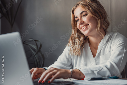 Happy young blonde business woman entrepreneur using computer looking at screen working in internet sit at office desk, smiling millennial female professional employee typing email on laptop at work