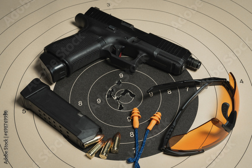 A shooting target with bullet holes in the center, a G19 pistol, goggles and earplugs, and a magazine with cartridges.