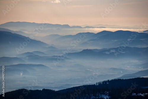 Panoramic view of magical blue mountain range of Lavanttal Alps, Carinthia, Austria. Valley is covered by mystical fog. Winter wonderland in Wolfsberg, Austrian Alps. Ski touring on Saualpe. Freedom