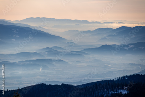 Panoramic view of magical blue mountain range of Lavanttal Alps, Carinthia, Austria. Valley is covered by mystical fog. Winter wonderland in Wolfsberg, Austrian Alps. Ski touring on Saualpe. Freedom