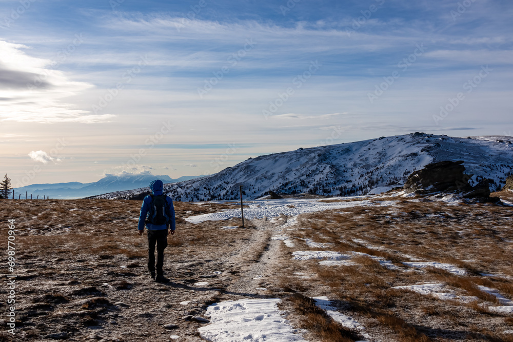 Man with backpack hiking in cold windy winter at Ladinger Spitz in the Saualpe mountain range, Lavantal Alps, Carinthia, Austria, Europe. Hike path along on alpine pasture. Tourism Wolfsberg