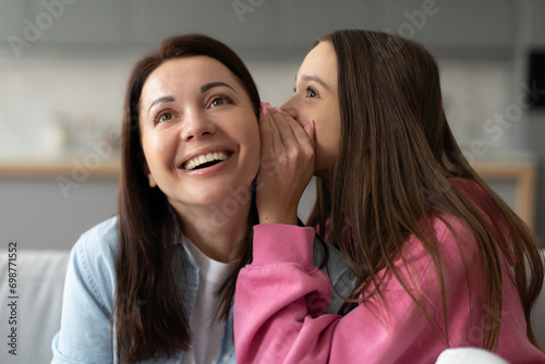 Mother enjoy time gossiping with daughter, girl whispering in ear of happy mom, teenager girl chatting with mummy. Concept of trustworthy relations photo