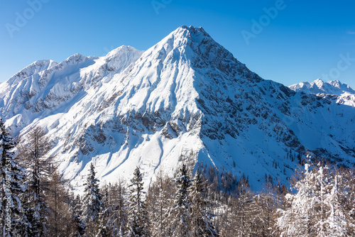 Scenic view on snow capped mountain peak of Mittagskogel (Kepa) in Karawanks, Carinthia, Austria, Europe. Winter wonderland in Austrian Alps. Snowshoe hiking through remote forest and snowy landscape