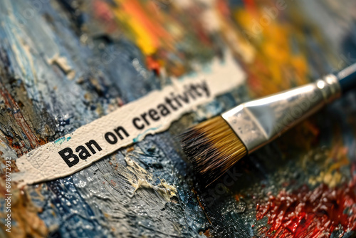 A paintbrush is seen resting on a piece of paper that features a ban on creativity. This image can be used to represent restrictions or limitations on artistic expression photo