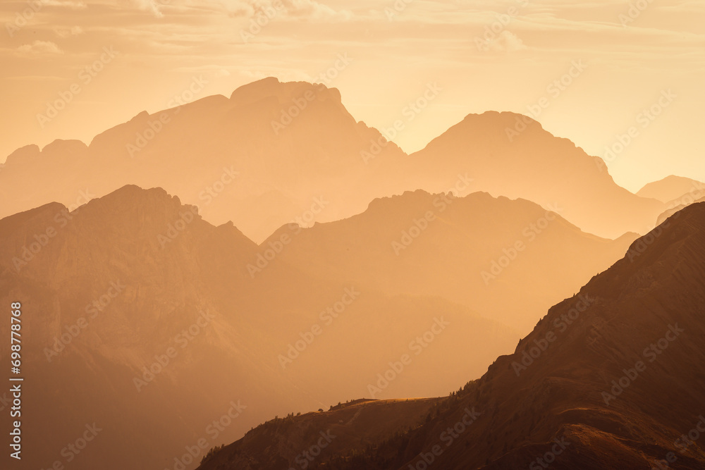 Italian Dolomites in colorful golden sunrise. Misty Alpine mountains in haze. Silhouettes of mountain peaks.