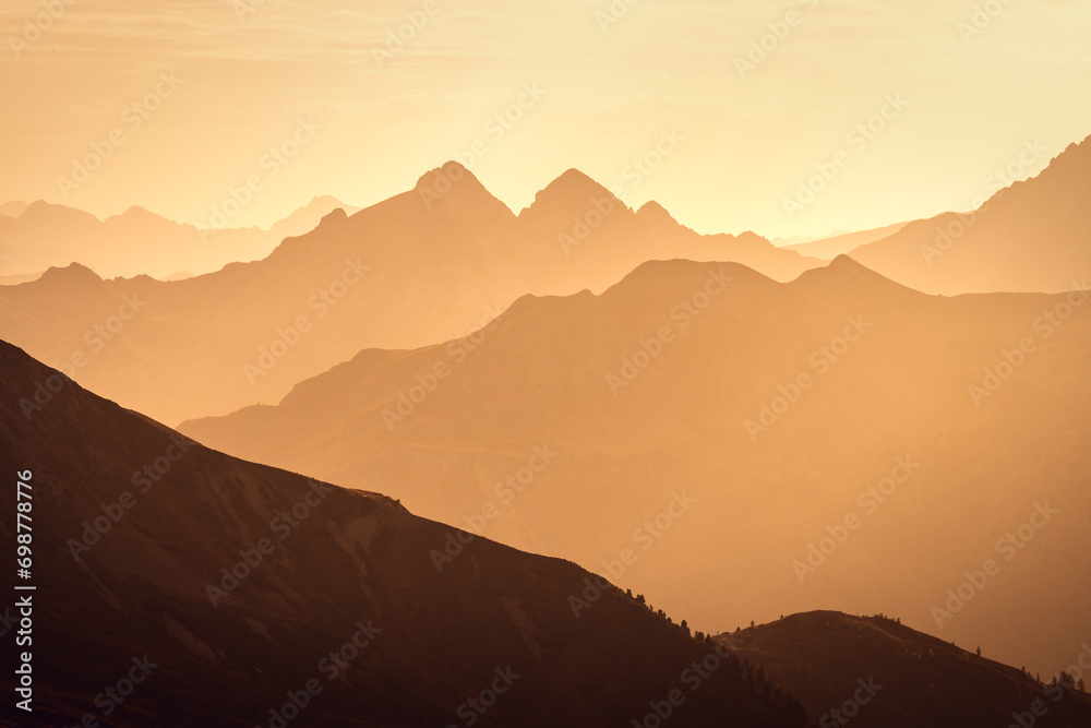 Italian Dolomites in colorful golden sunrise. Misty Alpine mountains in haze. Silhouettes of mountain peaks.