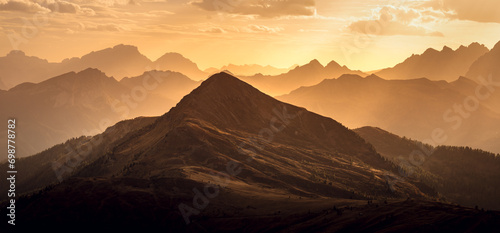 Italian Dolomites in colorful golden sunrise. Misty Alpine mountains in haze. Silhouettes of mountain peaks. 