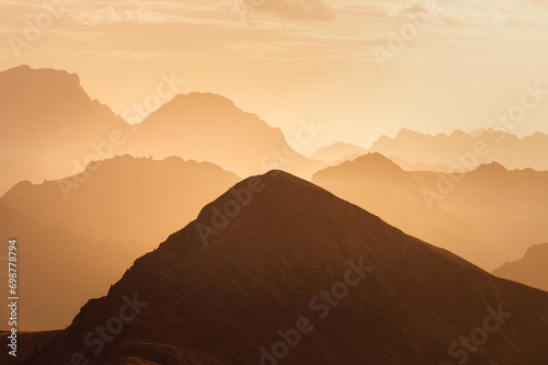 Italian Dolomites in colorful golden sunrise. Misty Alpine mountains in haze. Silhouettes of mountain peaks. 