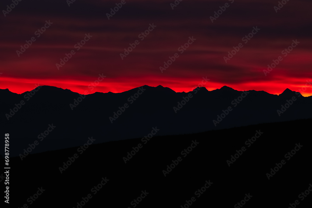 Dark red sky at Italian Dolomites with mountain peaks in distance. Twillight hour at Italian Alps. 