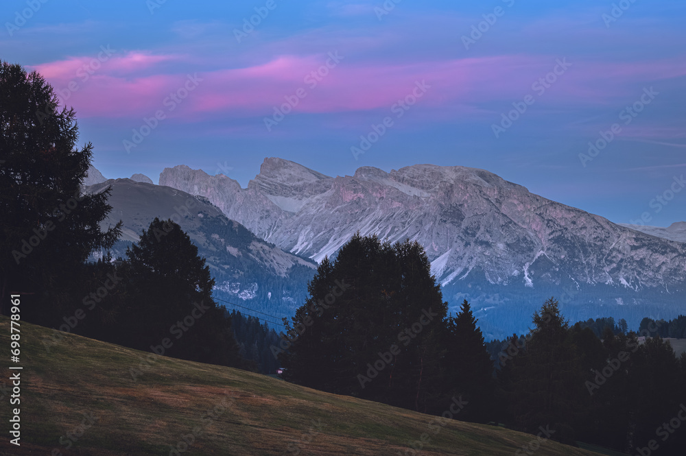 Stunning sunset at Langkofel with colorful sky at Italian Dolomites. Impressive Sassolungo mountain with Alpine lodges. 
