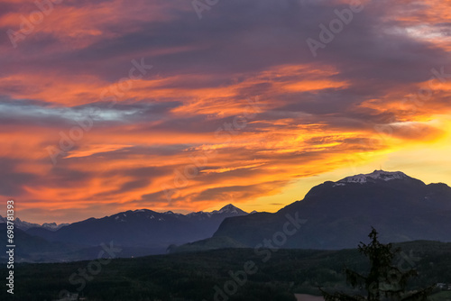 Scenic view of snow capped mountain peak Dobratsch at sunset seen from Taborhoehe in Carinthia, Austria, Europe. Sky has vibrant orange and pink colors with clouds swirling around summit. Serenity