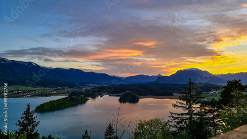 Panoramic sunset view on Lake Faak from Taborhoehe in Carinthia  Austria  Europe. Surrounded by high Austrian Alps mountains. Water surface reflecting soft sunlight. Remote alpine landscape in summer