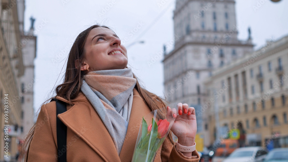 Fototapeta premium Portrait of a happy shade girl with a tulip in the background of the city in the cold season.