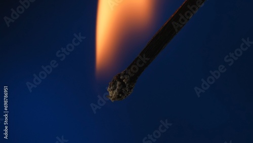 Macro shot of a burning match against a blue studio background. The flame of the burning match illuminates the dark space. The burning match is enveloped in an orange flame. photo