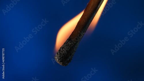 Macro shot of a burning match against a blue studio background. The flame of the burning match illuminates the dark space. The burning match is enveloped in an orange flame. photo