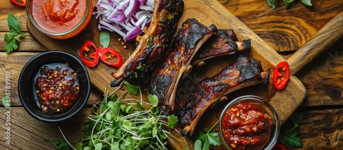 Wooden table showcasing top view of spicy condiments and grilled lamb ribs.