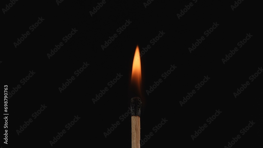 Macro shot of a burning match against a dark studio background. The flame of the burning match illuminates the dark space. The burning match is enveloped in an orang flame. Macro shot of a burning match against a dark studio background. The flame of the burning match illuminates the dark space. The burning match is enveloped in an orang flame.
