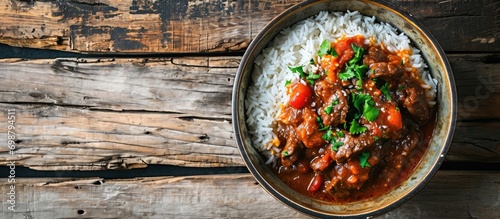 A horizontal view from above of a flavor-packed beef stew in tomato sauce, served with rice on an old wooden table, showcasing west African cuisine in a flatlay with empty space. photo