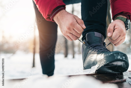 Unrecognizable male person tying shoelaces outdoors in winter.