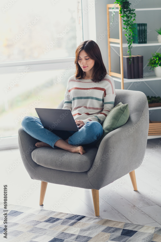 Full length vertical portrait of nice person barefoot sit chair use laptop write email bright modern flat inside Full length vertical portrait of nice person barefoot sit chair use laptop write email bright modern flat inside