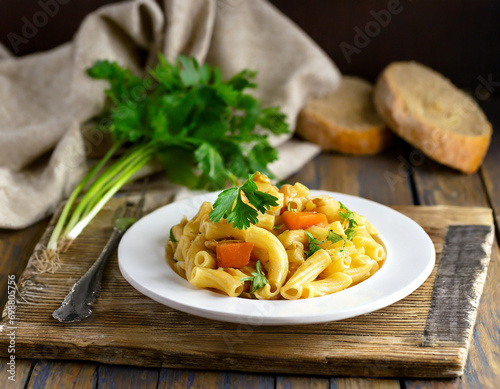 pasta with vegetables on a white plate stands on a wooden textured plank and textiles, in the background is soddy rustic bread and cilantro photo