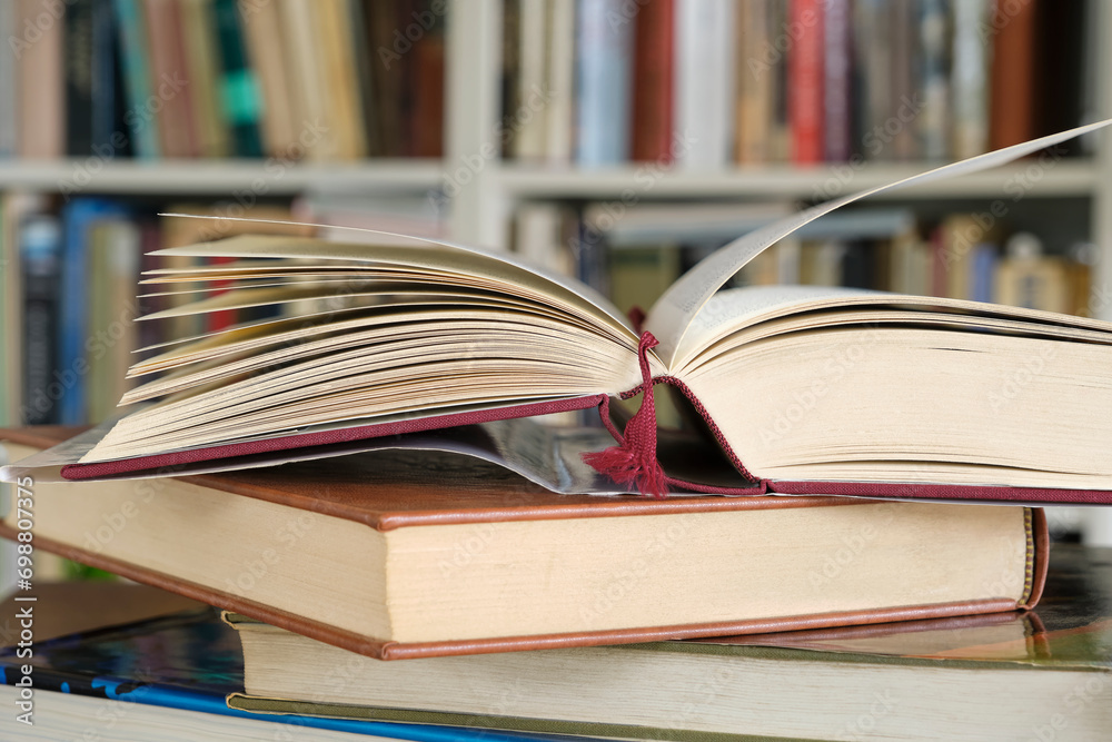 Open book or textbook on a pile of closed books in front of a bookcase in a library. Education learning concept. Image with selective focus. Open book or textbook on a pile of closed books in front of a bookcase in a library. Education learning concept. Image with selective focus.