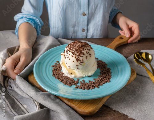 Ice cream on a blue plate with chocolate sprinkles on a table with gray textiles, next to a milkman on a wooden stand