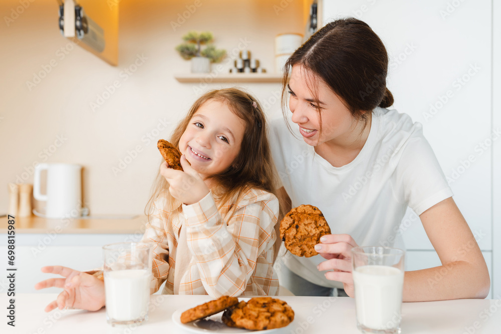Portrait beautiful smiling mother and cute little mother eating tasty cookies with milk on modern kitchen. Morning, breakfast, healthy lifestyle concept  